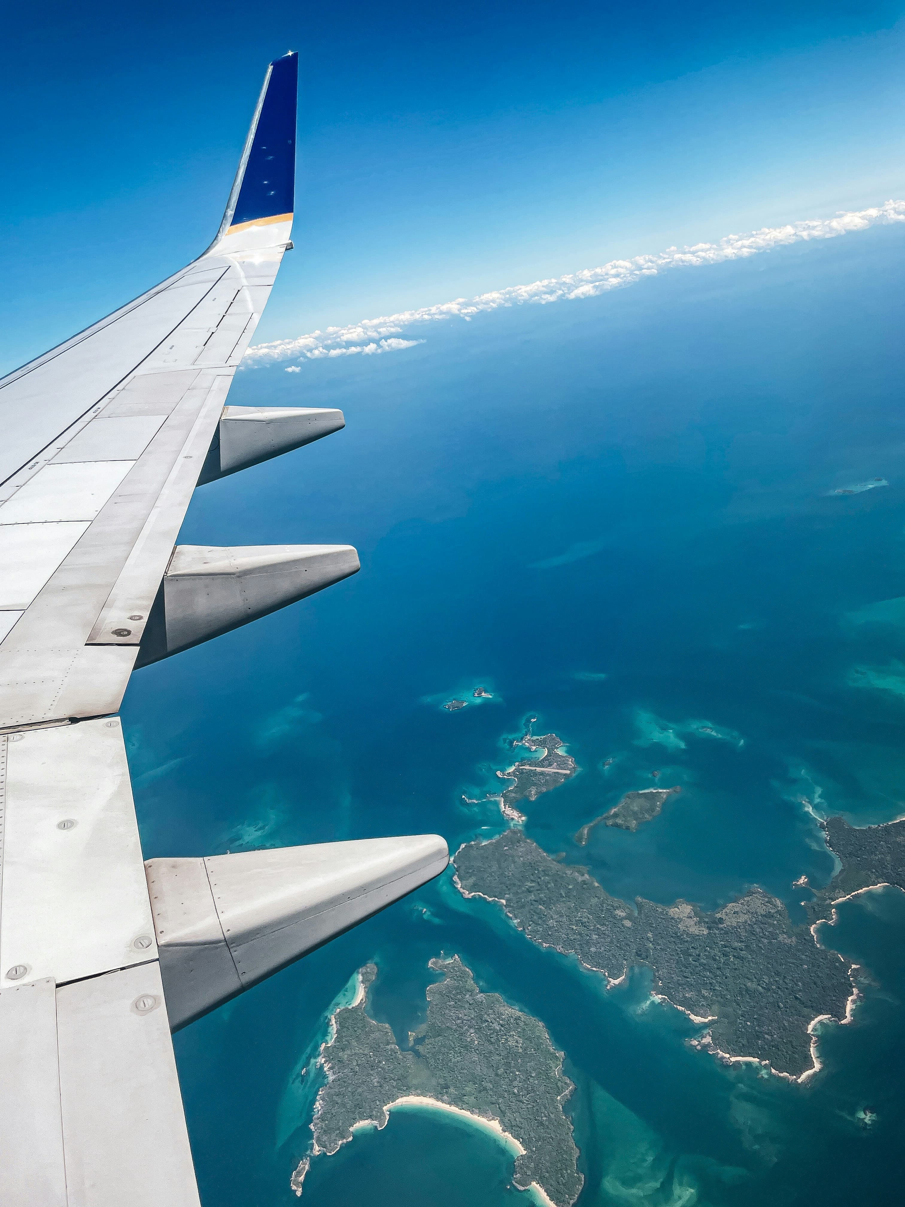 Luxury airplane wing view over turquoise ocean with tropical islands below during golden hour